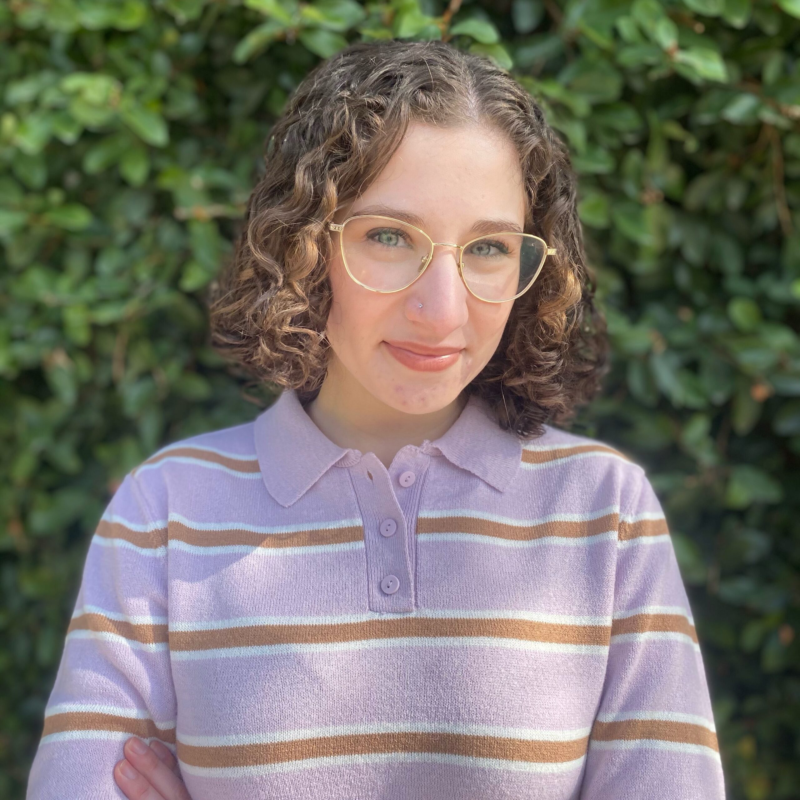 headshot of a young woman with curly brown hair and glasses wearing a lavender collared sweater